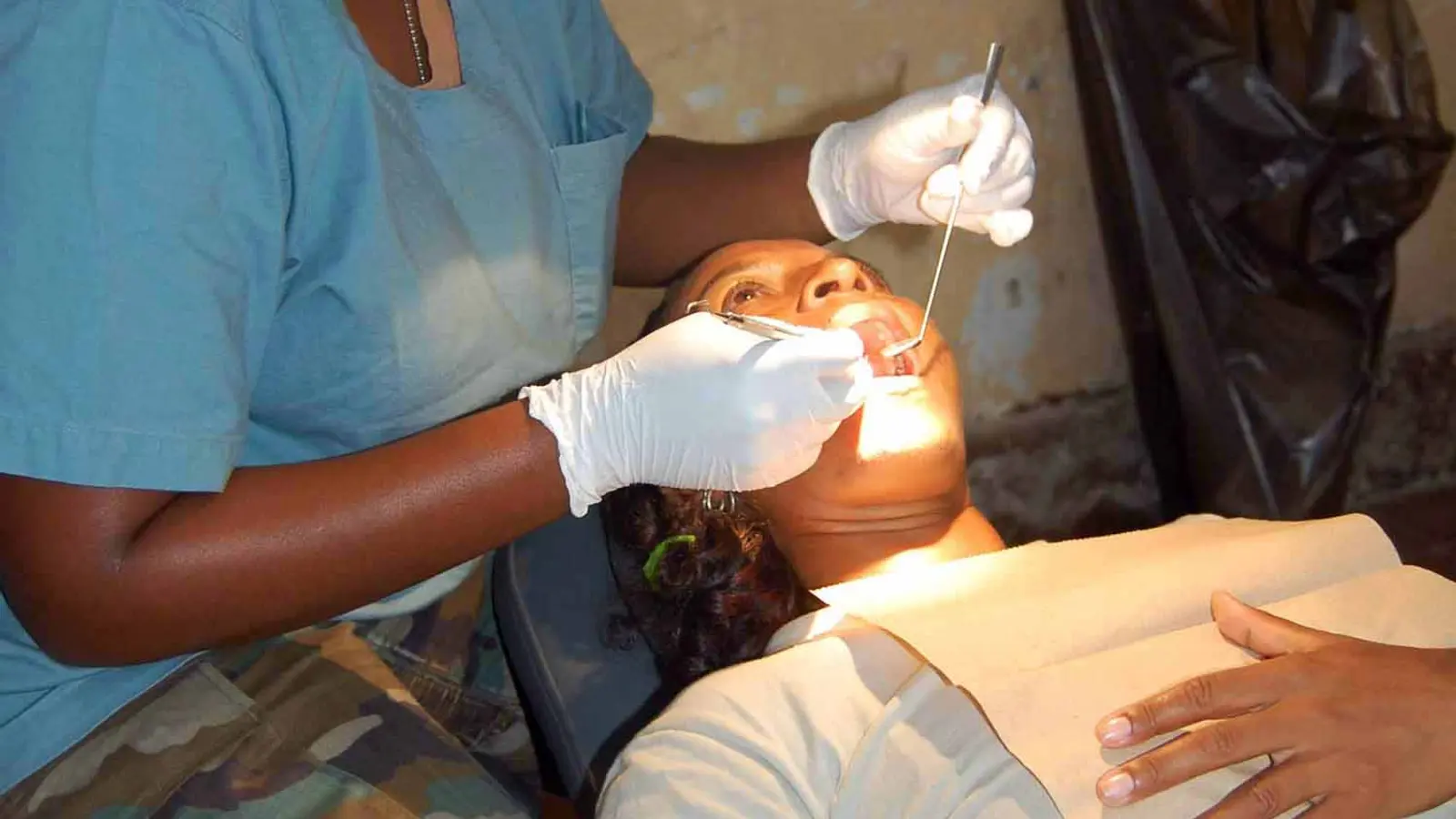 A dental hygienist in scrubs cleaning and scaling an adult patient’s teeth