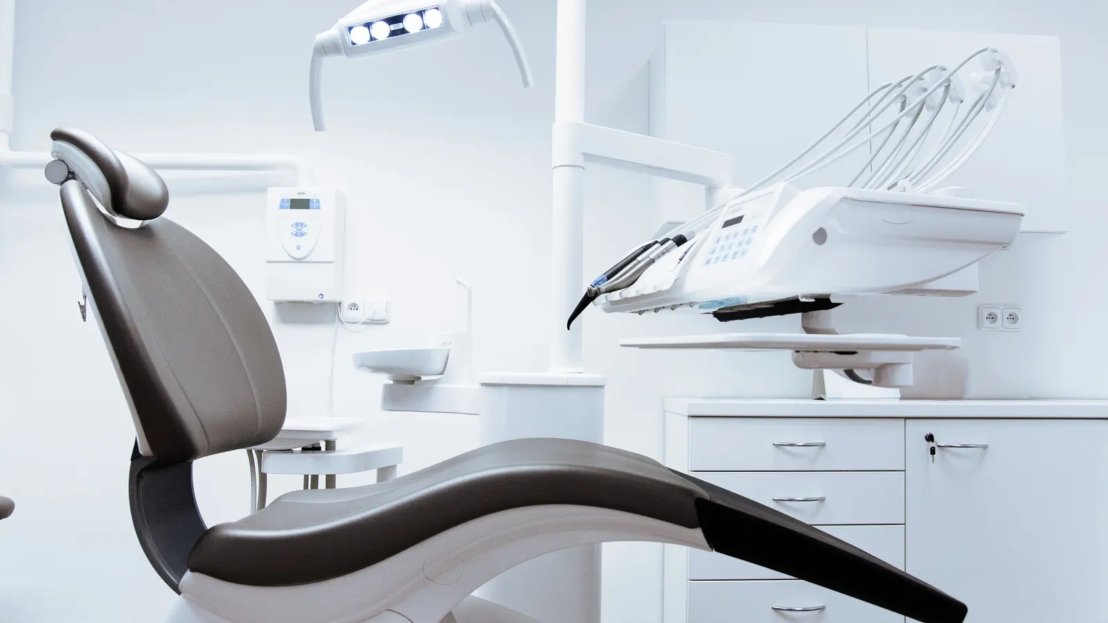 A clean, modern dental surgery with an empty treatment chair and instrument arm