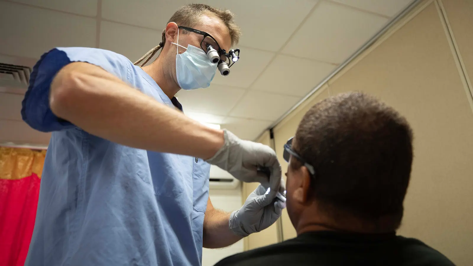 A dentist in scrubs examining a patient’s mouth with a probe