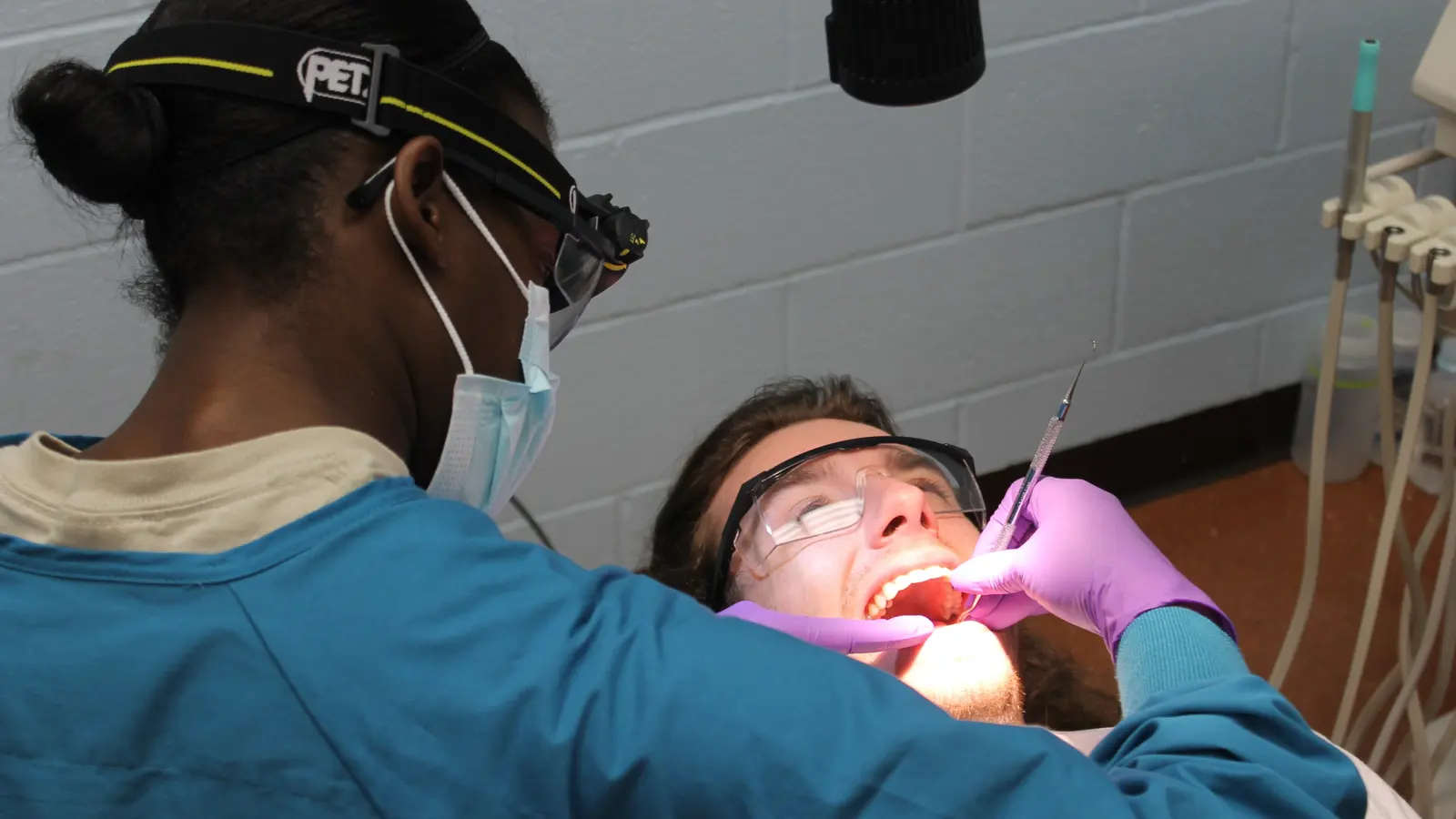 A dentist in scrubs and a headlamp treating a patient in the chair