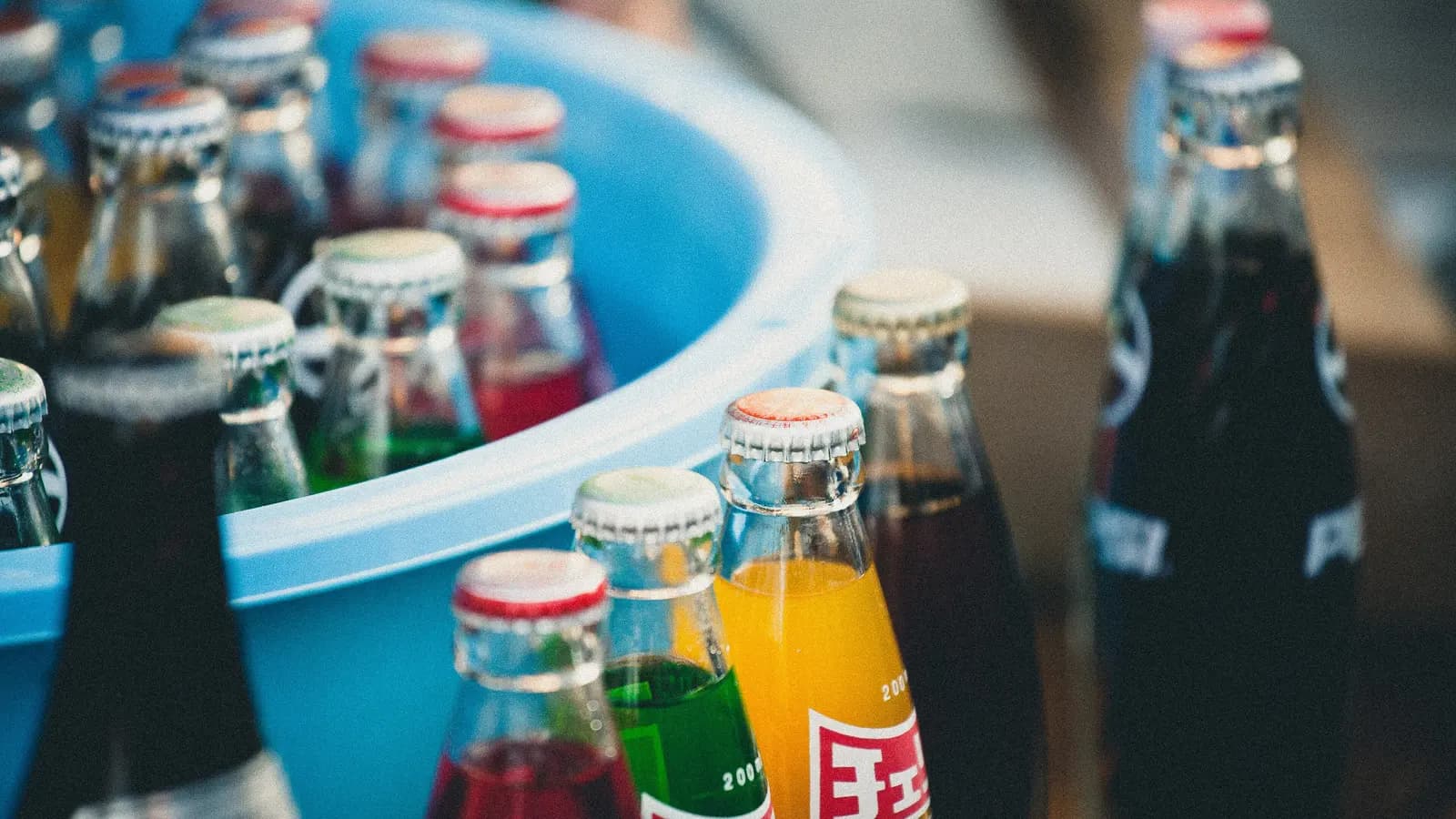 Glass bottles of brightly coloured soft drinks packed into a tub of ice
