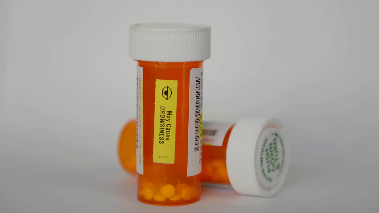 Two amber prescription bottles, one tipped over with tablets spilling out