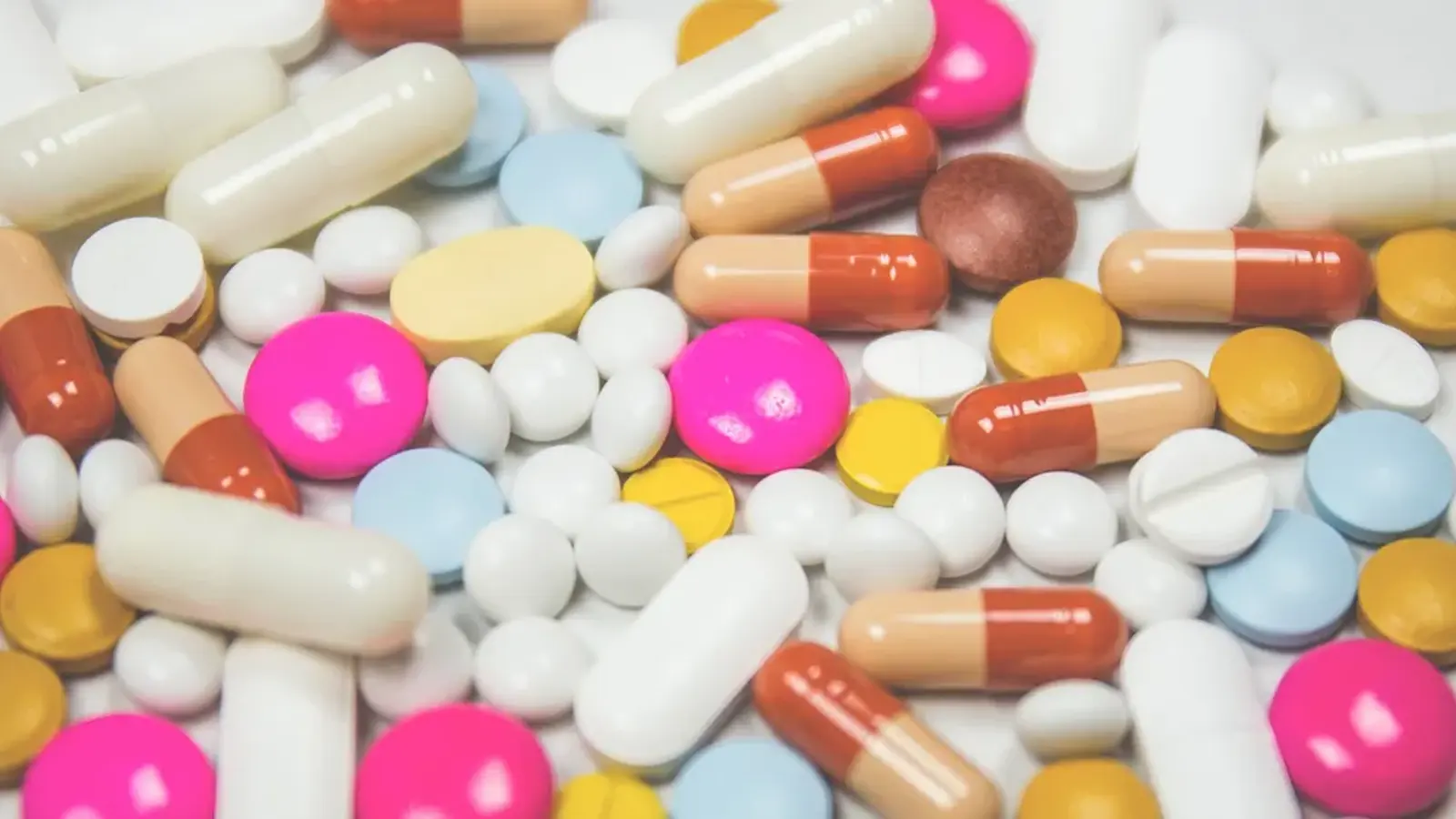 A close-up of assorted tablets and capsules in white, yellow, pink and orange