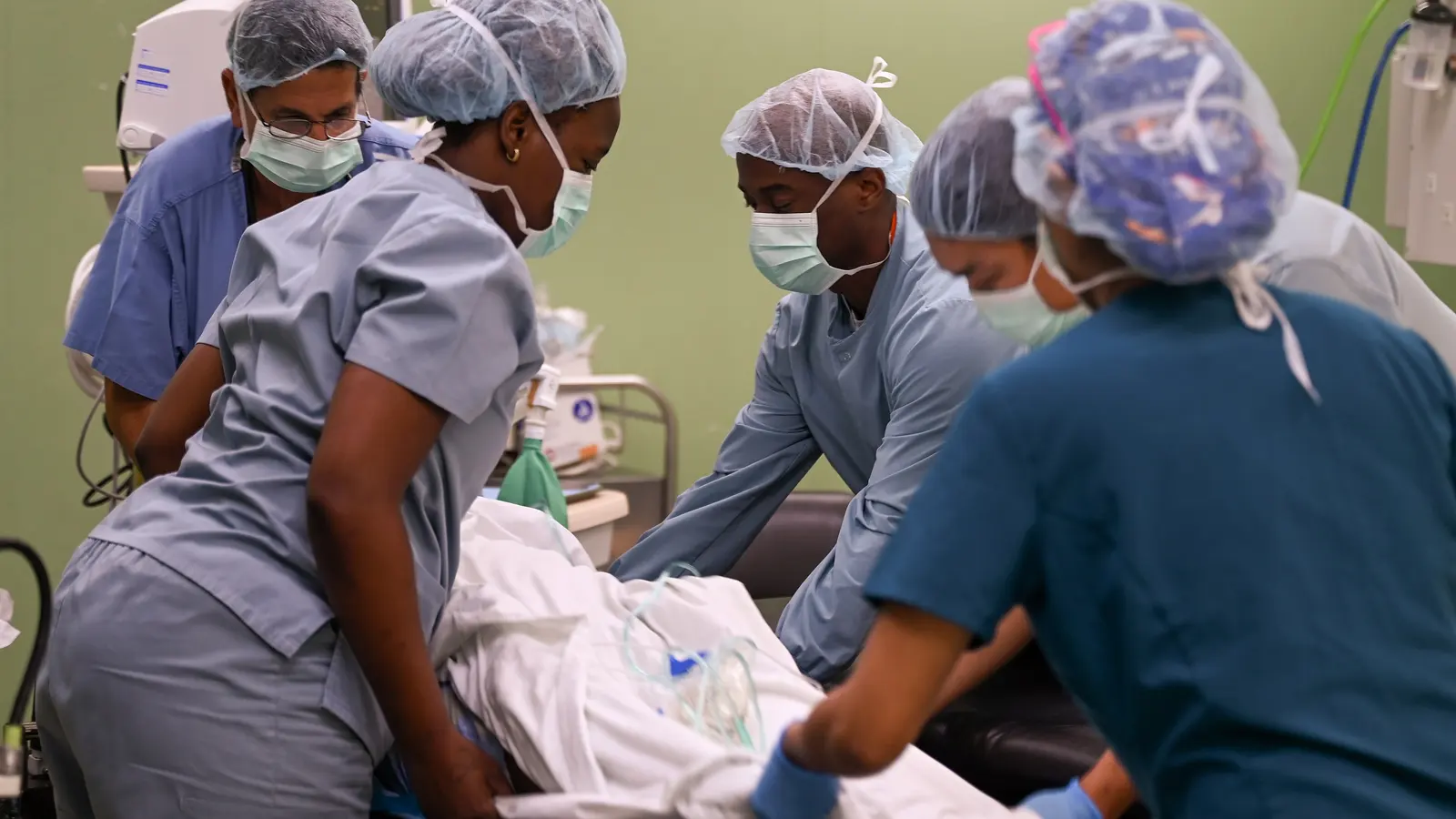 A team of clinicians in surgical scrubs and caps working together around a patient