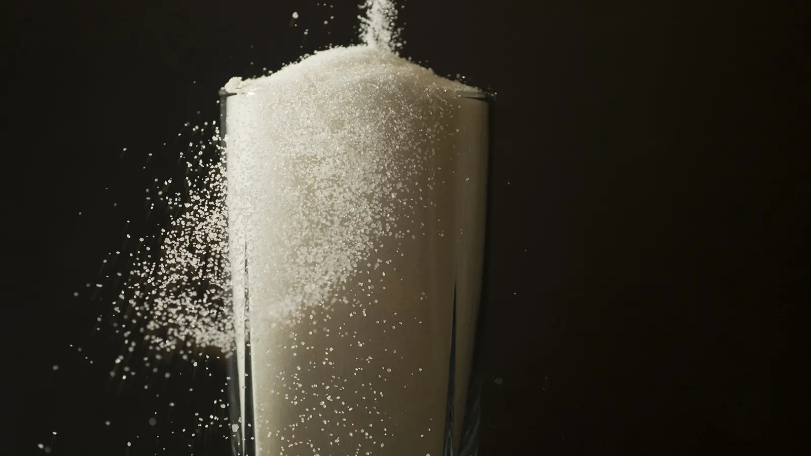 A stream of white sugar pouring into a glass against a dark background