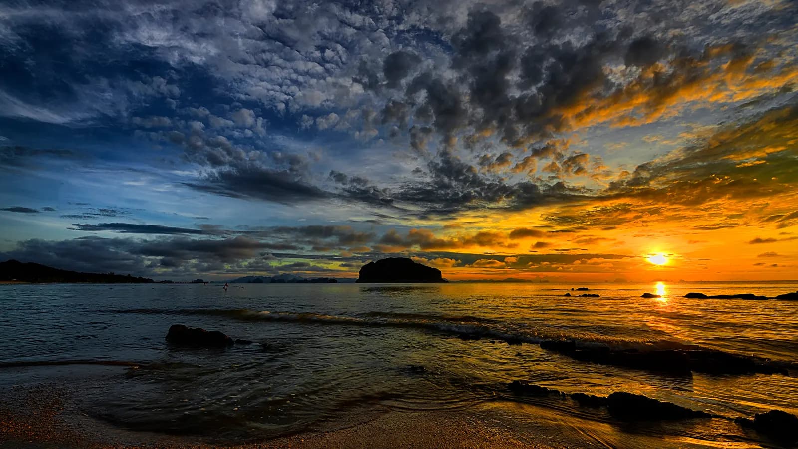 A deep orange sunset over calm water beneath a bank of dark cloud