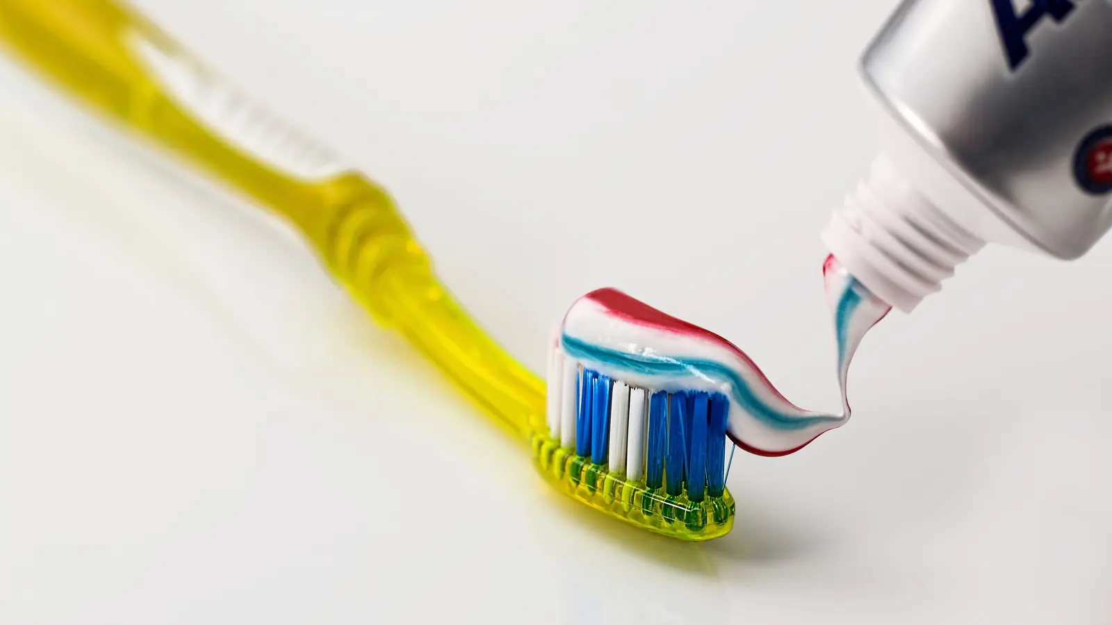 Striped toothpaste being squeezed onto a yellow toothbrush