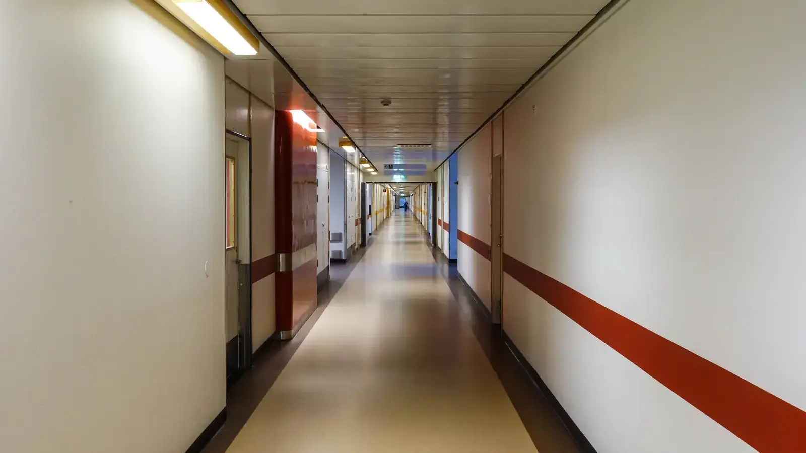 A long, empty hospital corridor receding towards a lit doorway