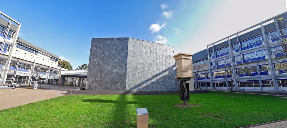 La Trobe University Health Sciences Building with the Charles La Trobe statue on the lawn, clear blue sky, daytime exterior.