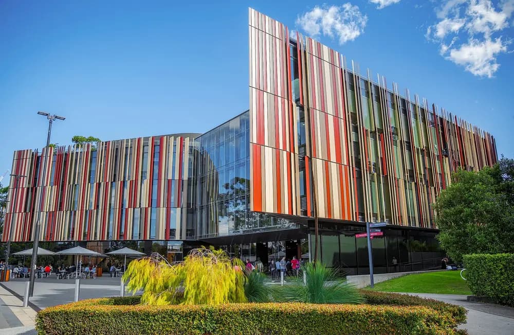 The iconic Macquarie University Library, a striking modern flagship building with colourful vertical fins, on the Macquarie University campus in Sydney, Australia, under a bright blue sky.