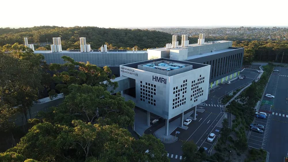 Golden-hour aerial exterior of the Hunter Medical Research Institute, a modern medical building on the University of Newcastle's Callaghan campus (host of the Joint Medical Program), surrounded by bushland.