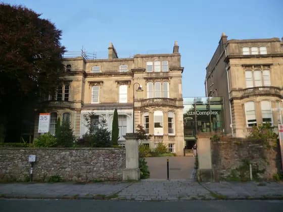 The main entrance to the Arts Complex at the University of Bristol. Two large limestone buildings are connected by a modern glass atrium, set in a courtyard with trees and bushes Bristol — The main entrance to the Arts Complex at the University of Bristol. Two large limestone buildings are connected…