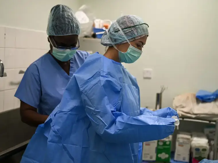 Two clinicians in surgical scrubs and caps gowning up before a procedure